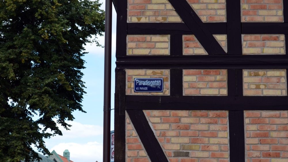 Sign with the text “Paradisgatan” in the Paradis neighborhood, attached to the wall of a brick house with half-timbering.